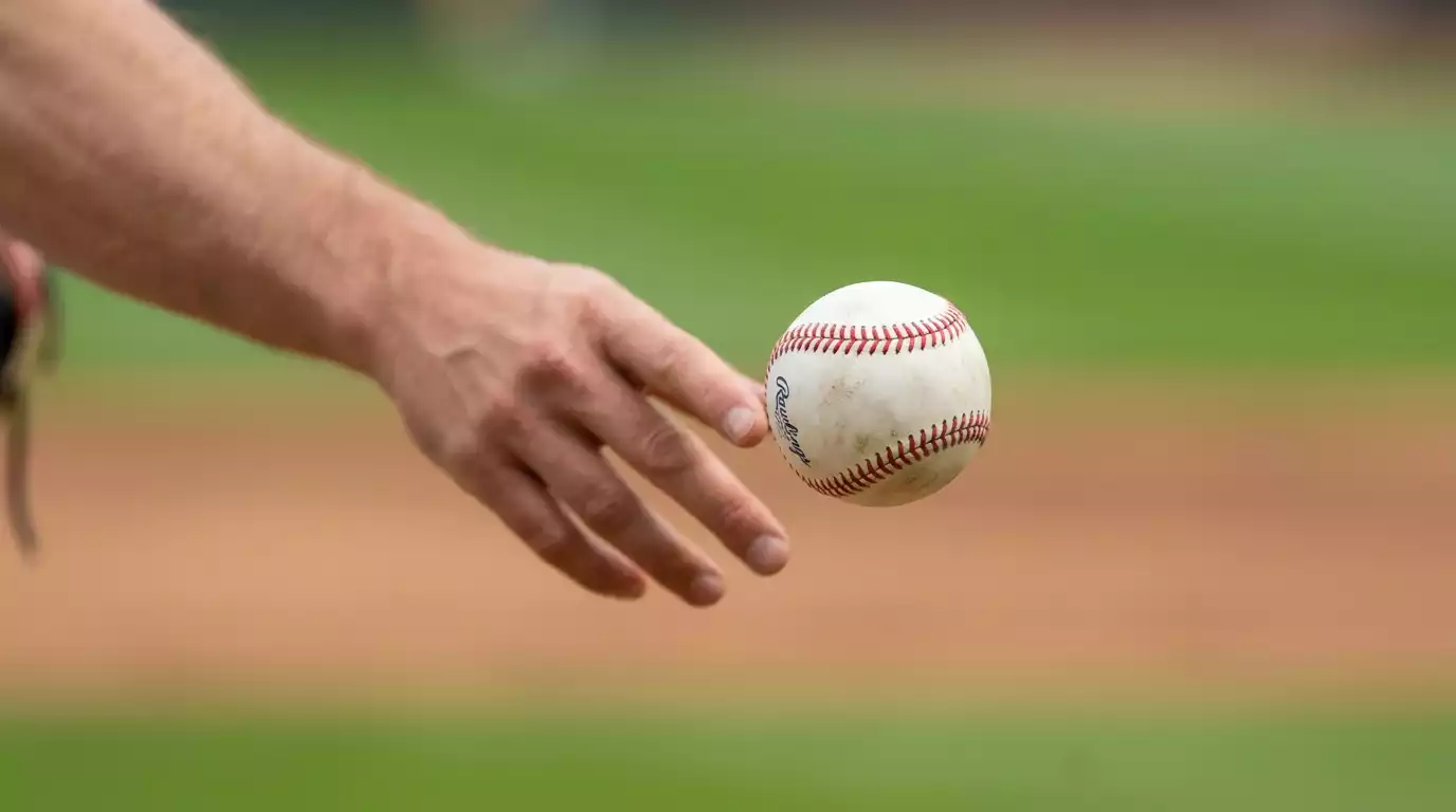 Close-up sports photo of a regulation white Major League Baseball with red stitching mid-flight just after release, slight motion blur, blurred green outfield grass behind